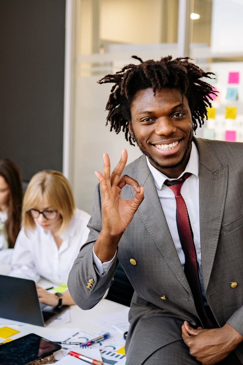 Smiling businessman signaling OK, working with diverse team in modern office.